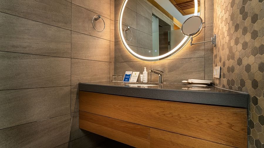 A Modern vanity with a chic round mirror and warm lighting - Sarovar Premiere, Srinagar